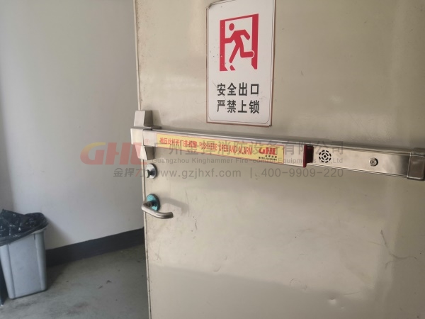 逃生門鎖警示標識，與錚亮的不銹鋼鎖體形成強烈對比